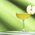 Apple pie alcoholic cocktail beverage with vodka, apple liqueur, cinnamon syrup.. Light green background, hard light, shadow pattern. Minimalistic style