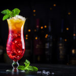 Aruba Ariba summer cocktail drink with vodka, white rum, orange, lemon and pineapple juice, grenadine syrup, dark bar counter background