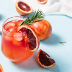 Delicious Blood Orange Bourbon Smash Cocktail on light blue background. Summer cocktails, refreshing drinks, low alcohol mocktail concept