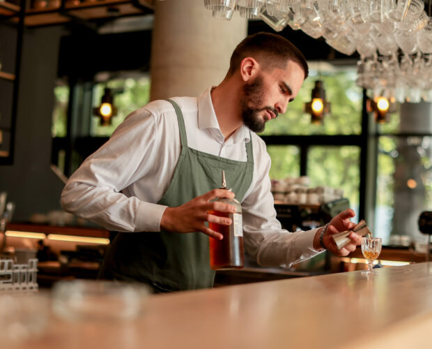 In a lively bar setting, a confident bartender mixes a fresh cocktail, showcasing his expertise with a bottle in hand, ready for the night's rush