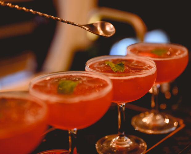 The young bartender is making a cocktail and decorating it in a martini cocktail glass for beautiful at a nightclub bar. Vodka, cocktail, alcohol, beverage, restaurant, relax concept.